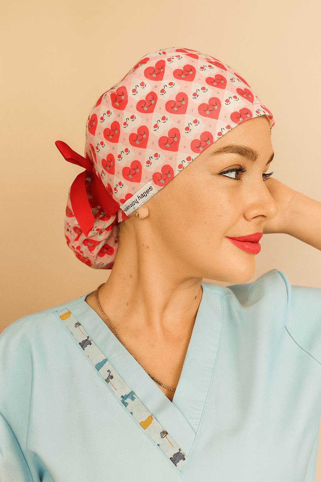 Smiling woman wearing a vibrant scrub cap covered in red and pink heart designs with cute smiley faces. The cap features a red ribbon tied at the back and a visible label reading "everyday beauty." Ideal for healthcare professionals, nurses, and doctors seeking stylish, comfortable, and expressive scrub caps. Photo showcases cheerful personality and premium stitching detail, perfect for Valentineโs Day or themed workwear.