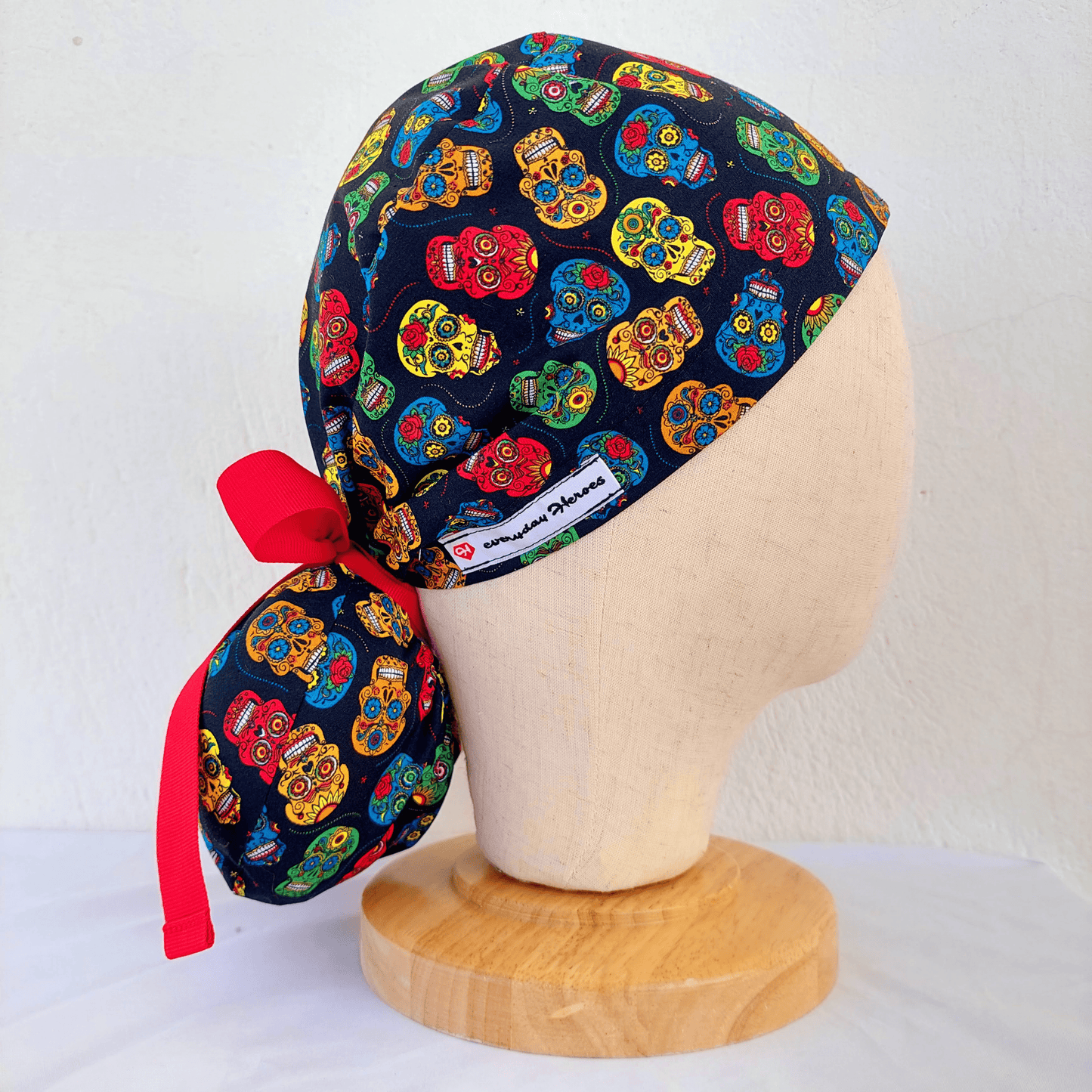  Left side of a mannequin wearing a scrub cap ponytail with small colorful skulls and a separate pounch on it for the ponytail that hold the long hair and ties with red ribbons