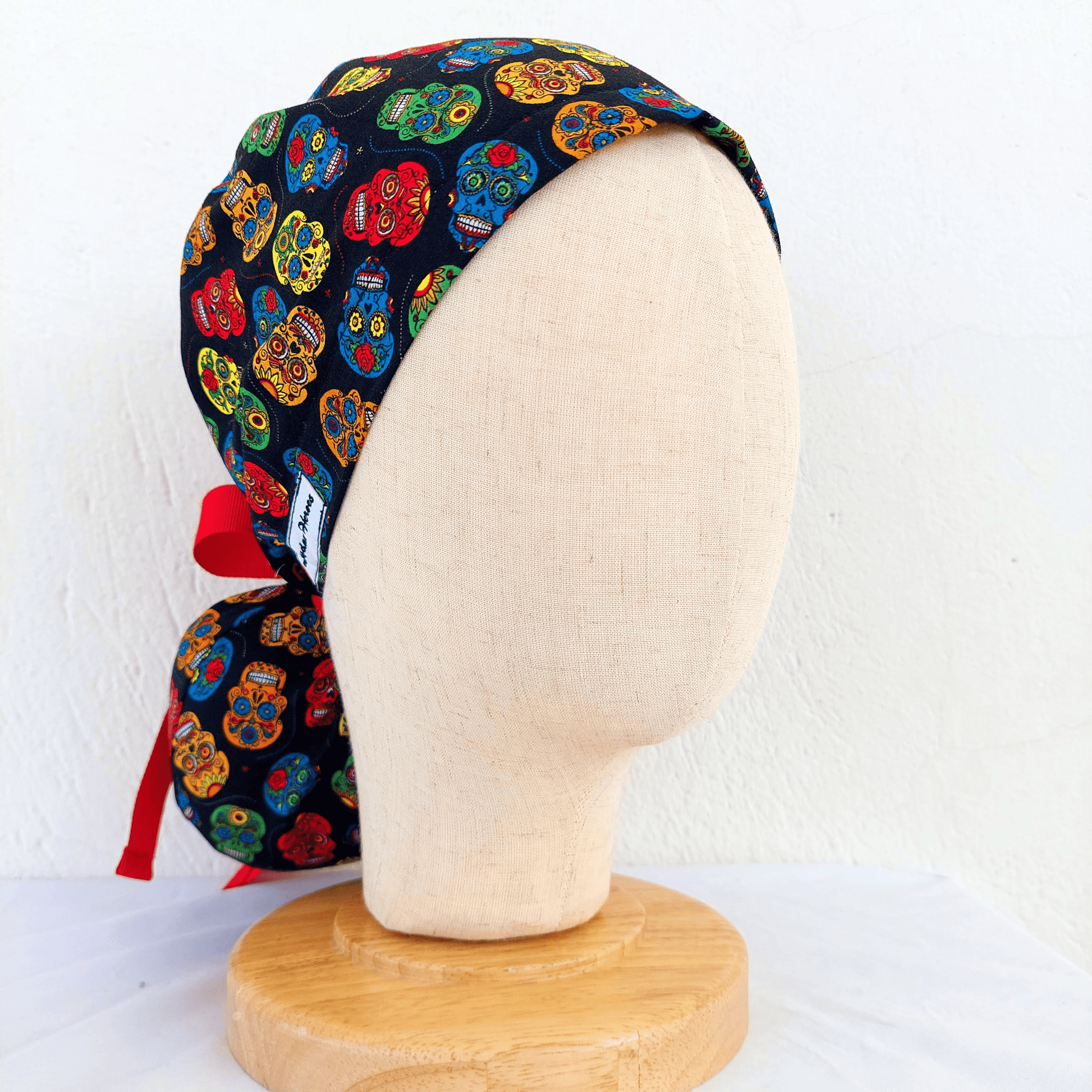 mannequin wearing a scrub cap ponytail with small colorful skulls and a separate pounch on it for the ponytail that hold the long hair and ties with red ribbons