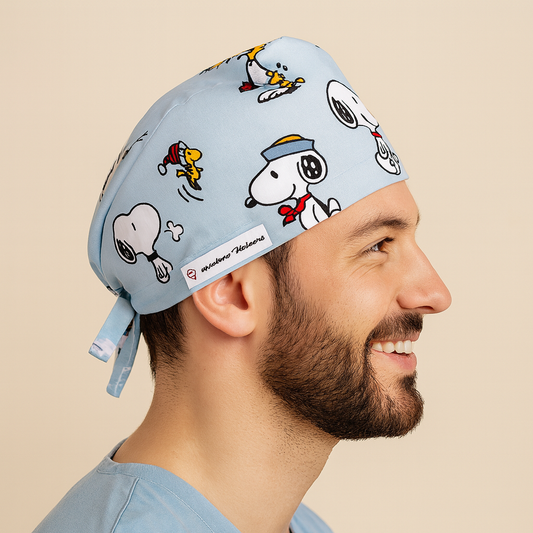 Smiling male doctor wearing a light blue cartoon scrub cap featuring Snoopy and Woodstock print. Adjustable and comfortable men’s surgical hat perfect for surgeons, doctors, or pediatric staff. A fun, professional, and thoughtful custom gift for doctors in the OR or clinic.