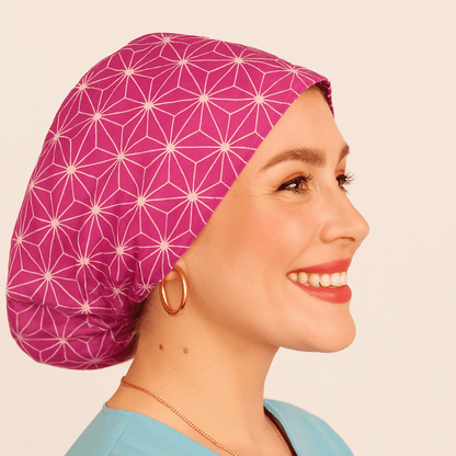 a woman wearing  apink scrub cap with abstract asanoha cotton print, the style is euro scrub hat its adjustable and she is smilling .