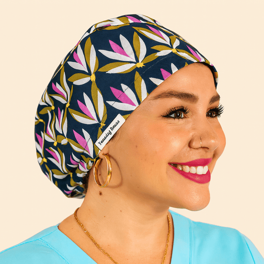 Smiling woman wearing a navy floral euro scrub cap with pink and water lliysprint. Custom satin-lined surgical hat for nurses, surgeons, and estheticians. Lightweight, stylish, and professional scrub cap providing comfort and hair protection during long shifts.